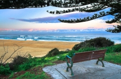 A bench overlooks a scenic section of coastline at Tuross Head, as seen at sunset. New South Wales, Australia.